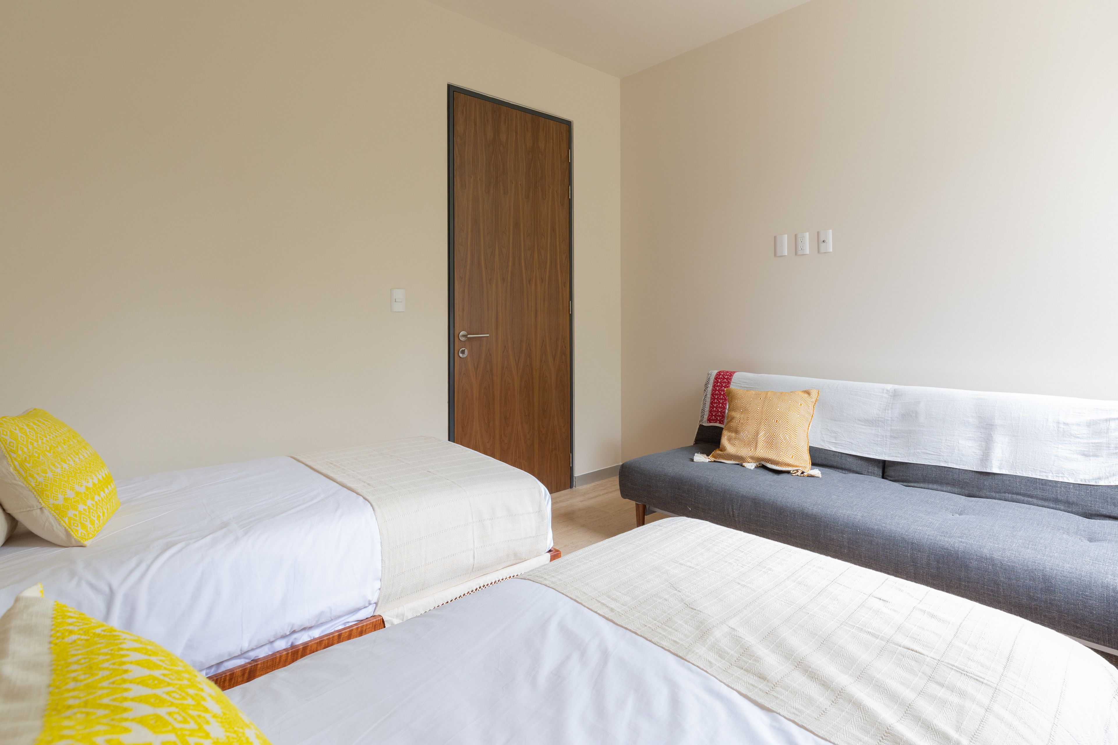 A hotel room with two beds, a sofa, and a wooden door.