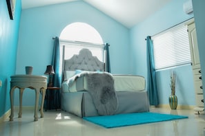A bedroom with a bed, a nightstand, a lamp, a vase, and a window with curtains.