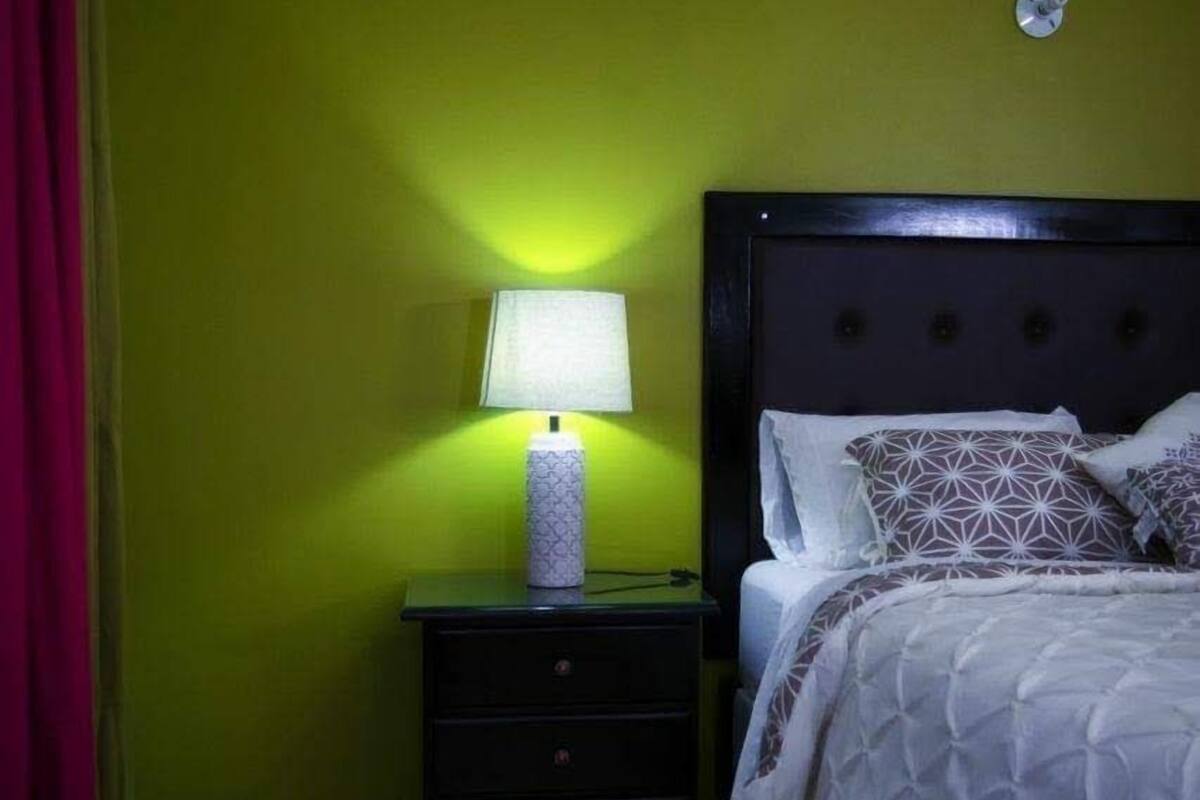 Une chambre avec un lit, une table de chevet avec une lampe et des murs verts.