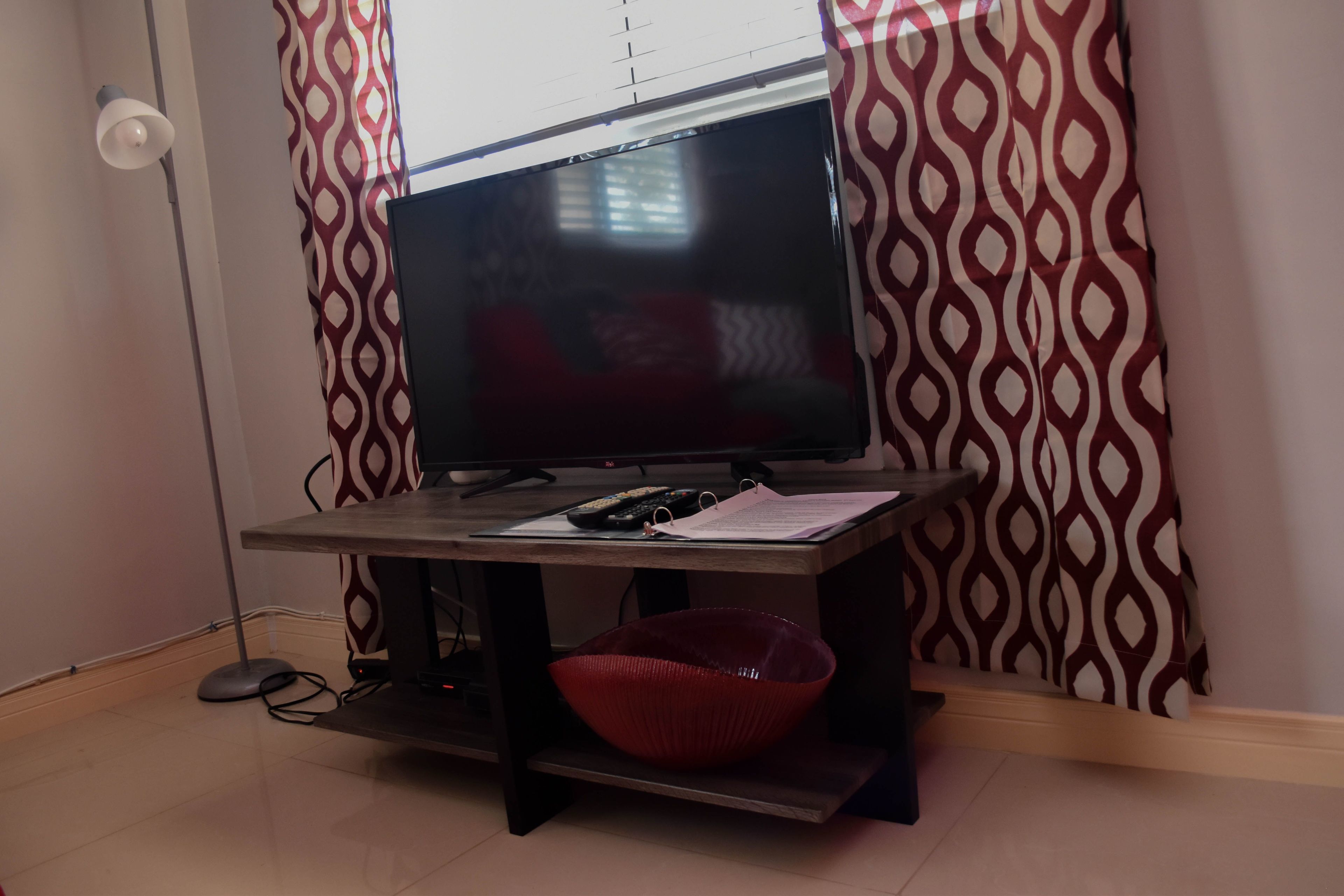 A room with a television on a stand, a red bowl, and patterned curtains.