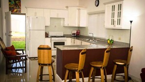 Una cocina con gabinetes blancos, una isla central con taburetes, una estufa y un refrigerador.