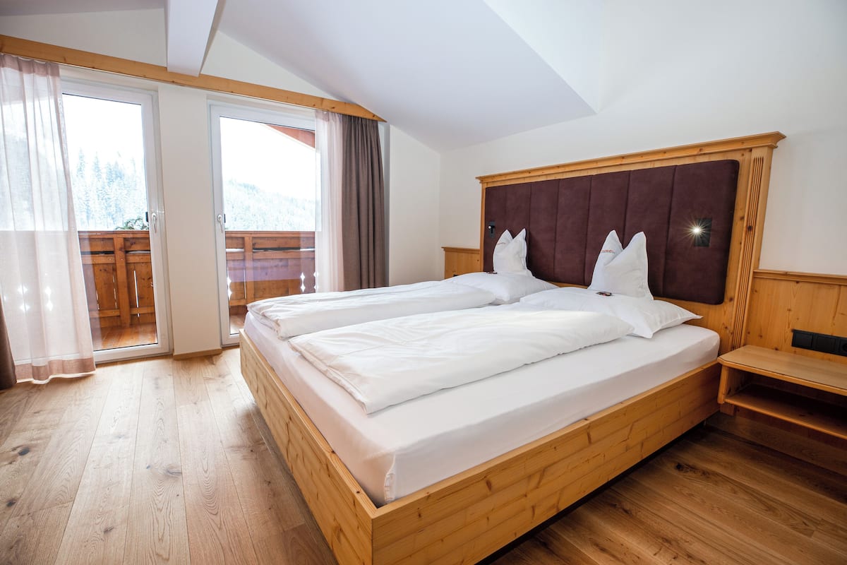A double bed with a wooden headboard, a wooden floor, and a balcony with a wooden railing.