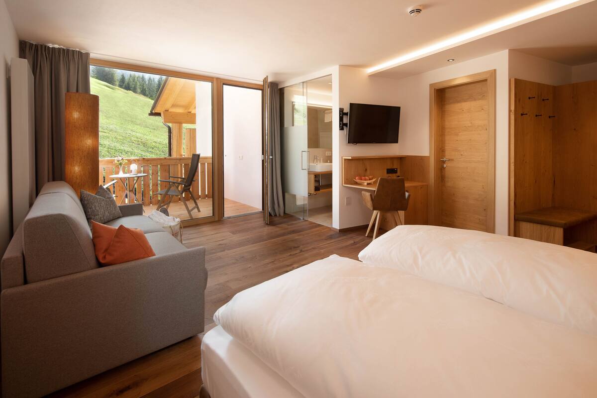 A modern hotel room with a sofa, two beds, a dining area, and a TV.