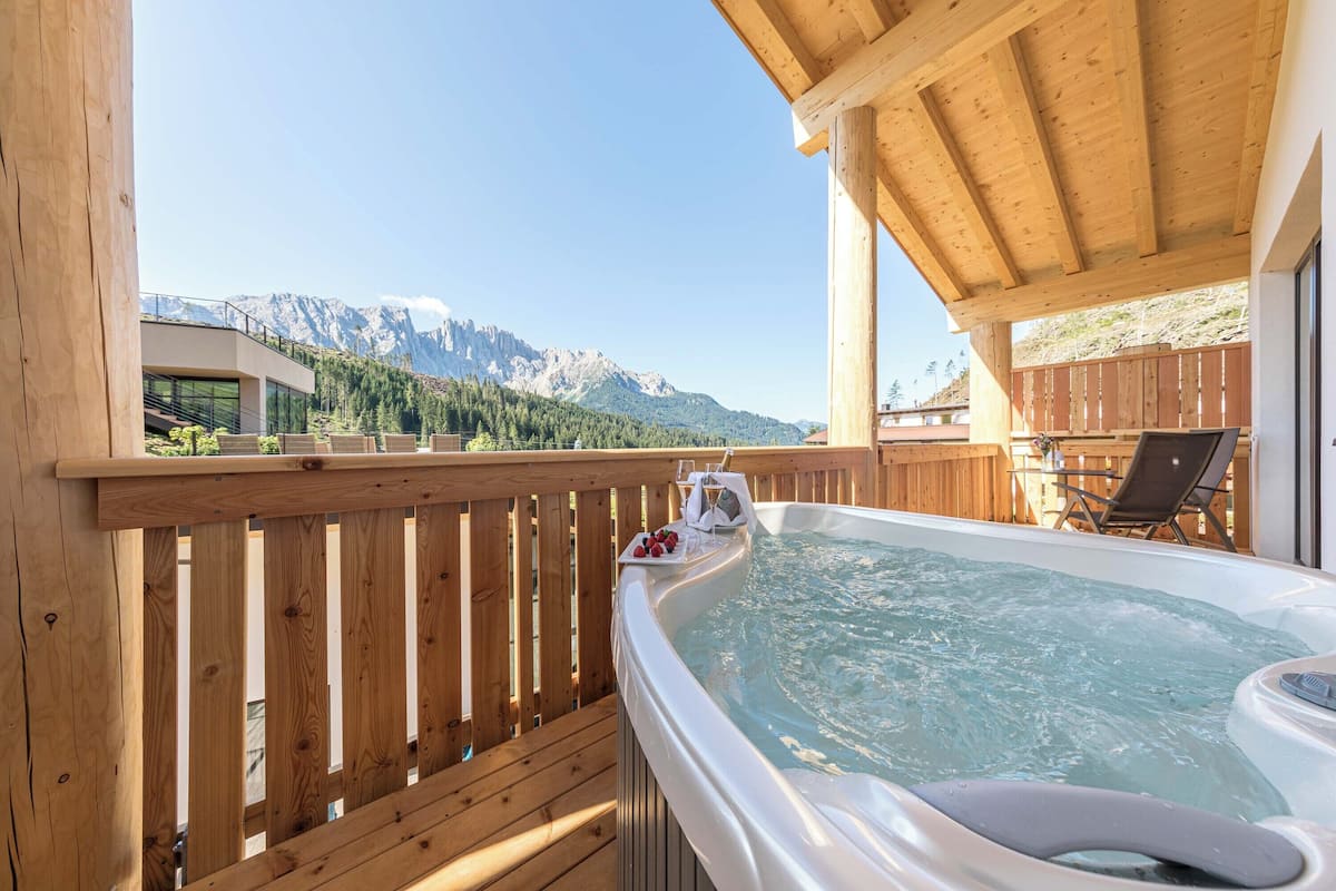A wooden deck with a hot tub, wooden chairs, and a mountain view.