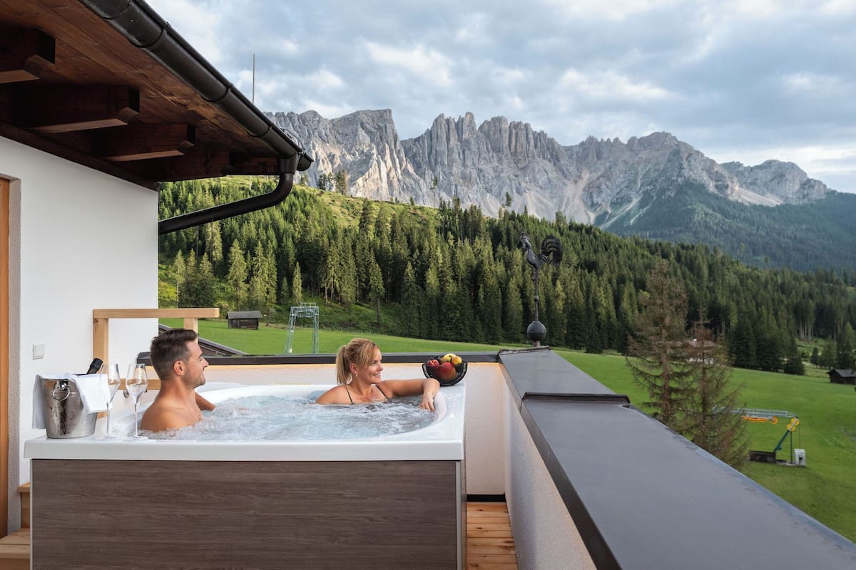 A hot tub with a mountain view, wooden deck, and a bucket with fruits.