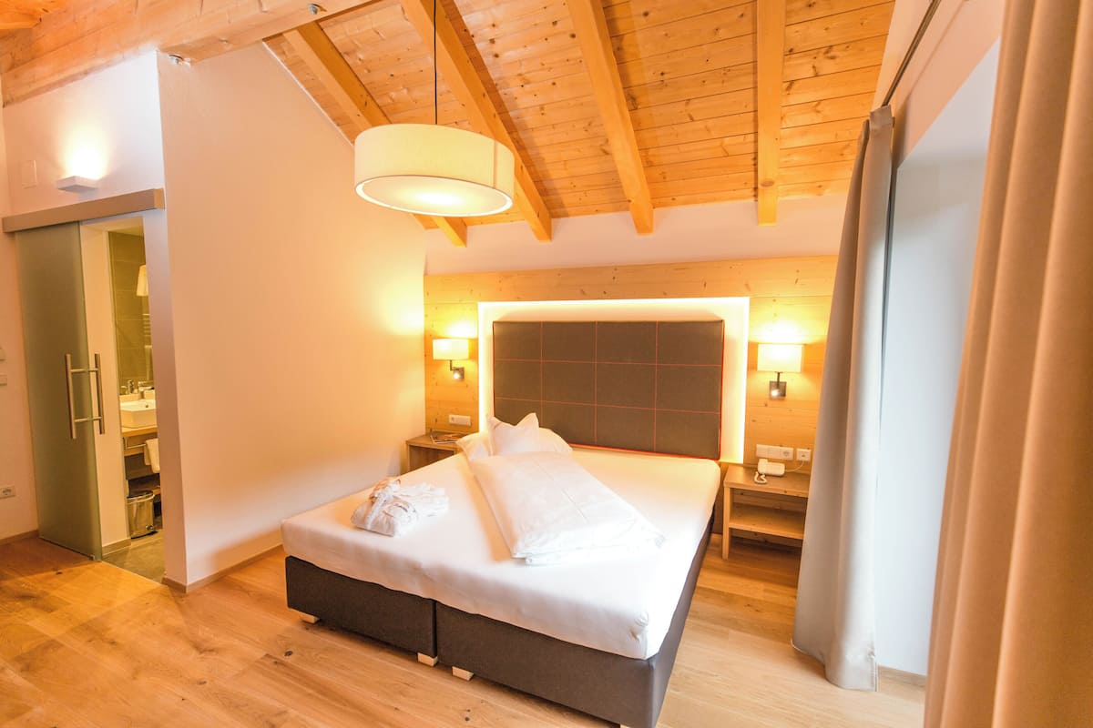 A bedroom with a wooden ceiling, a large bed with white linens, two bedside tables with lamps, and a wooden floor.