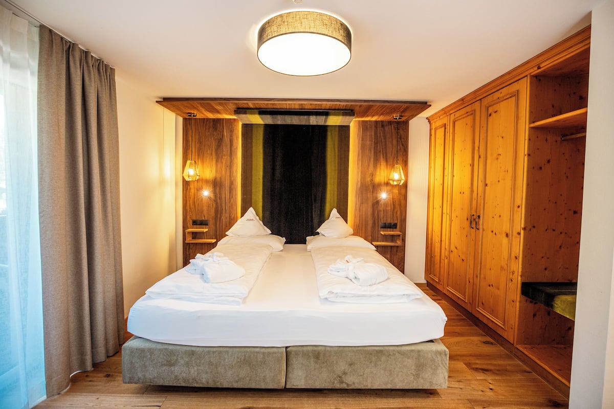 A hotel room with a large bed, wooden wardrobe, and two wall-mounted lamps.