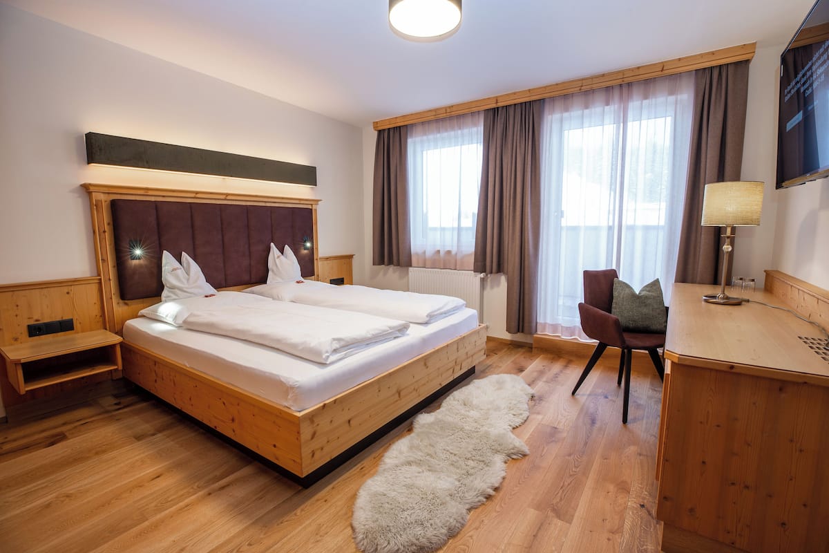 A hotel room with a wooden bed, a desk, a chair, and a large window with curtains.