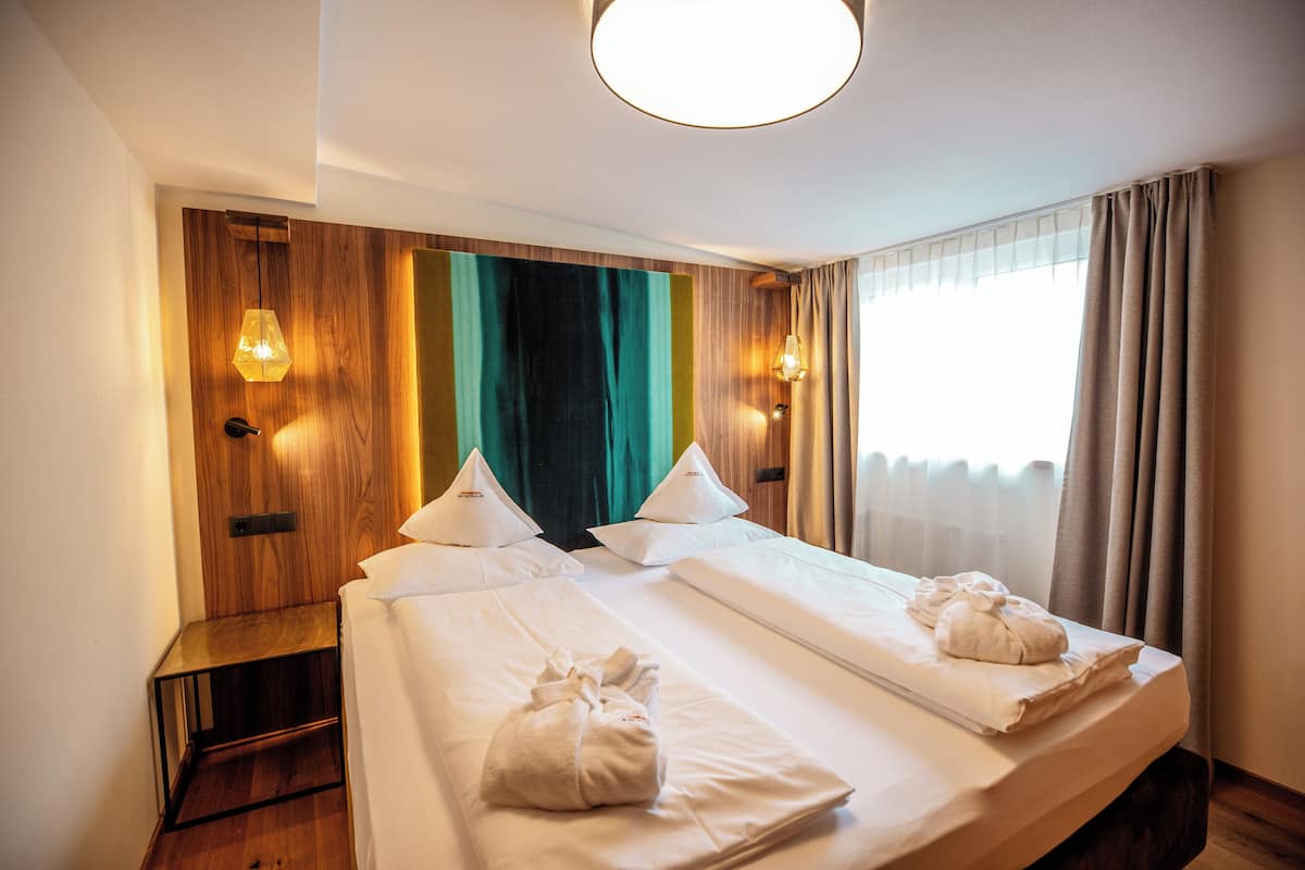A hotel room with two beds, wooden paneling on the walls, and a large window with curtains.