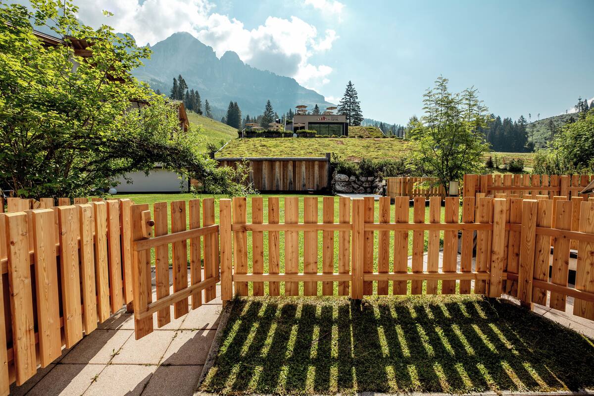 A wooden fence with a grassy area in front, a building with a mountain backdrop, and a clear sky.