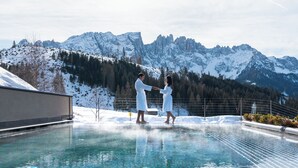 A couple in white robes by a clear pool with a snowy mountain backdrop. - Moseralm Dolomiti Hideaway (Nova Levante)