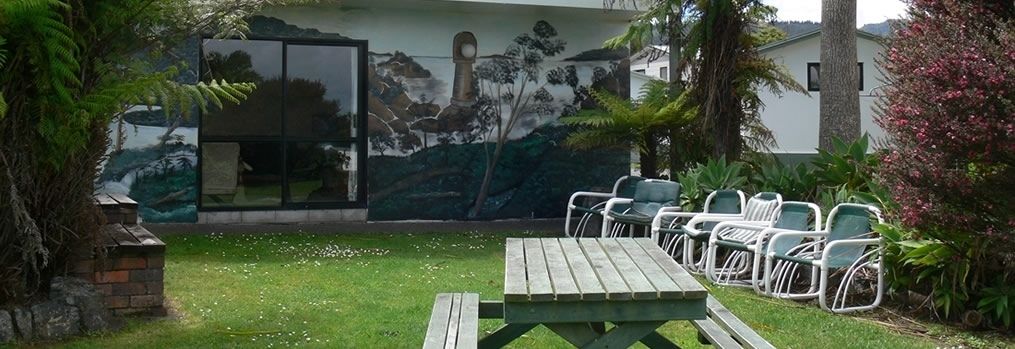 A patio with a wooden table and chairs, a mural on the wall, and a grassy area.