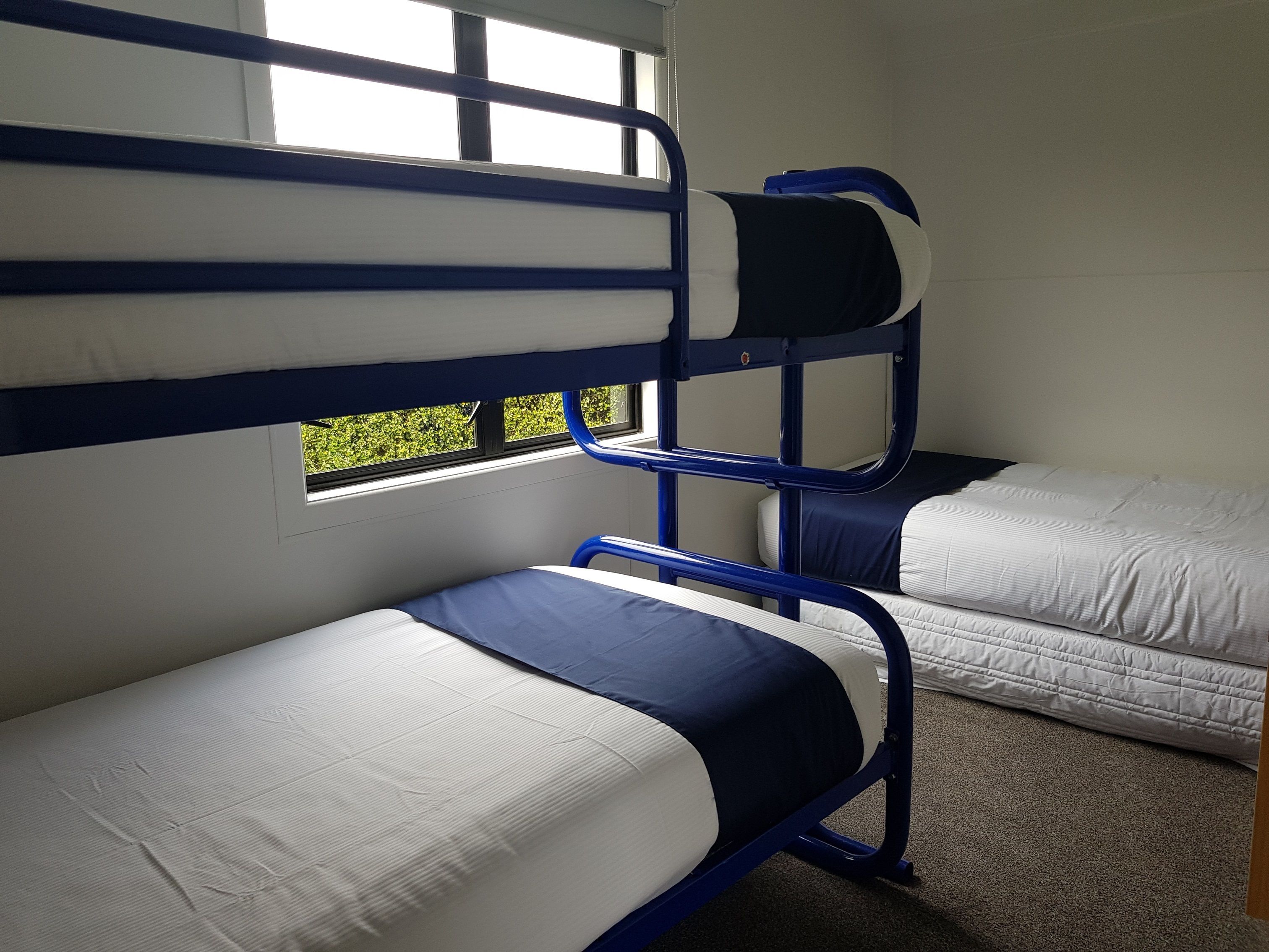 Een slaapkamer met stapelbed, een vloerbedekking en uitzicht op groen.