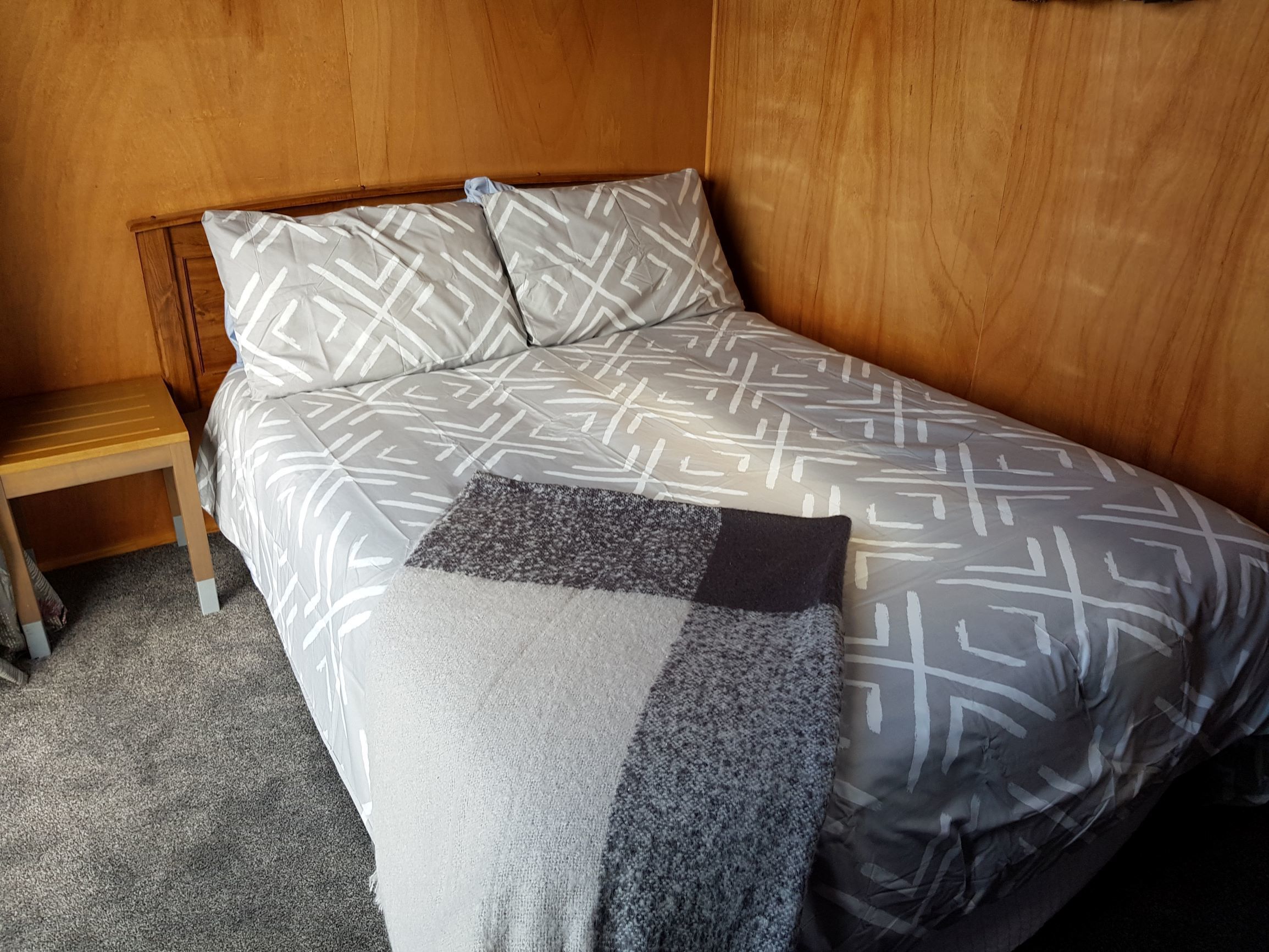 Un lit avec une couvre-lit à motifs géométriques, une petite table de chevet et un plaid gris et noir.