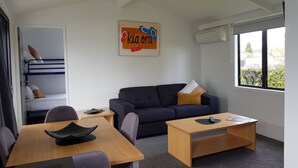 Un salon moderne comprenant un canapé, une table basse, une table à manger avec des chaises, un lit superposé et une fenêtre donnant sur un espace verdoyant.