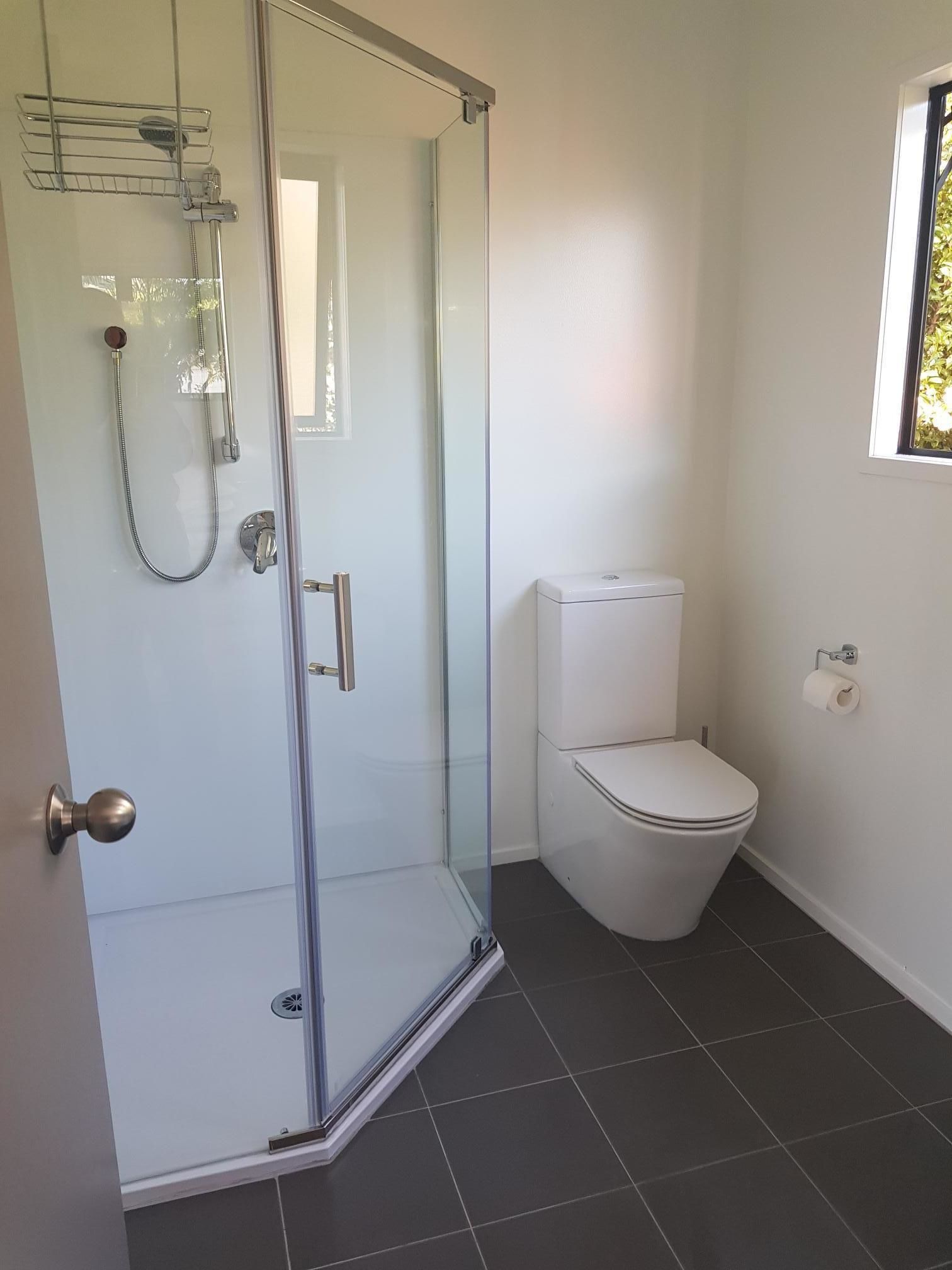 A modern bathroom with a glass shower enclosure, a white toilet, and a window providing natural light.