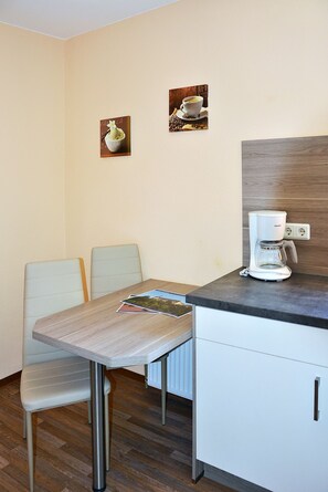 A small kitchenette with a coffee maker, two chairs, a table, and two framed pictures on the wall. - Apartment 6 - House Erna (Bad Wildungen)