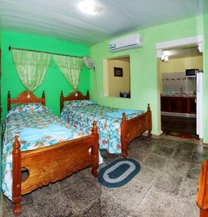 Ein Zimmer mit zwei Holzbett, einer grünen Wand, einer Klimaanlage und einer kleinen Küchenzeile.
