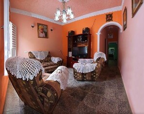 Ein Wohnzimmer mit zwei Sofas, einem Fernseher, einer Chandelüster und einem gerahmten Bild an der Wand.
