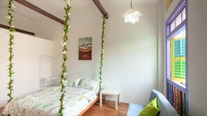 A bedroom with a bed, a small table, a sofa, and a window with colorful shutters. - Secret Garden Homestay (George Town)
