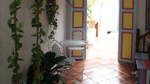 A room with a tiled floor, a chair, a hanging plant, and a door with colorful panels. - Secret Garden Homestay (George Town)