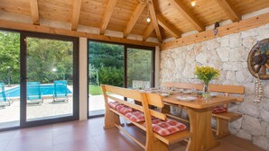 A wooden dining table with benches, a stone wall, and a view of a swimming pool.