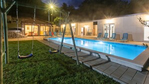 A swimming pool with a swing set, a covered seating area, and a building with doors and windows.