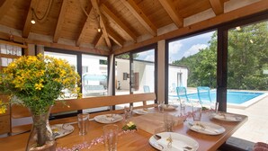 A dining area with a wooden table set for a meal, large windows, and a view of a swimming pool.