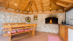 A cozy room with a stone wall, a fireplace, wooden benches, and a kitchen area.