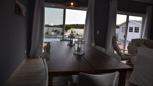 Ein Essbereich mit einem Holztisch, weißen Stühlen und Blick auf ein Schwimmbecken und ein Haus.
