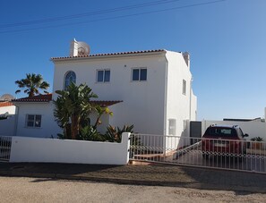A white two-story house with a red-tiled roof, a small balcony, and a car parked in the driveway.