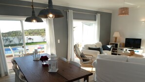Ein modernes Wohnzimmer mit einem Holzespeisetisch, weißen Stühlen, einem weißen Sofa und einem Fernseher.