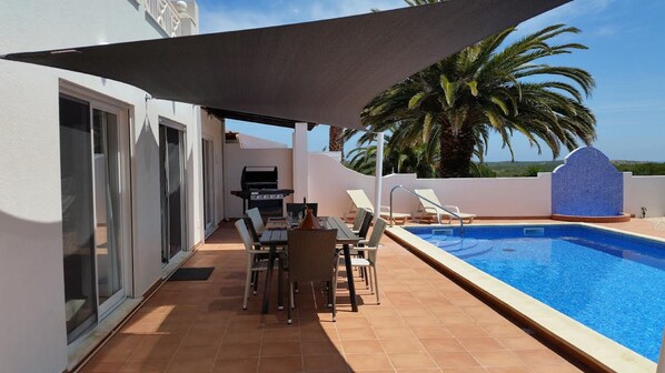 An outdoor patio with a pool, a grill, and lounge chairs.
