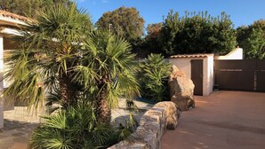 A residential area with a stone wall, palm trees, a garage, and a house with a tiled roof. - The ideal place to relax, Beautiful villa with all the comforts (Sainte-Lucie de Porto-Vecchio)