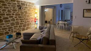 A living room with a stone wall, a sofa, a glass coffee table, and a dining area with a table and chairs. - The ideal place to relax, Beautiful villa with all the comforts (Sainte-Lucie de Porto-Vecchio)