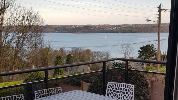 Un balcon avec une table et des chaises, donnant sur une étendue d’eau et une côte lointaine.