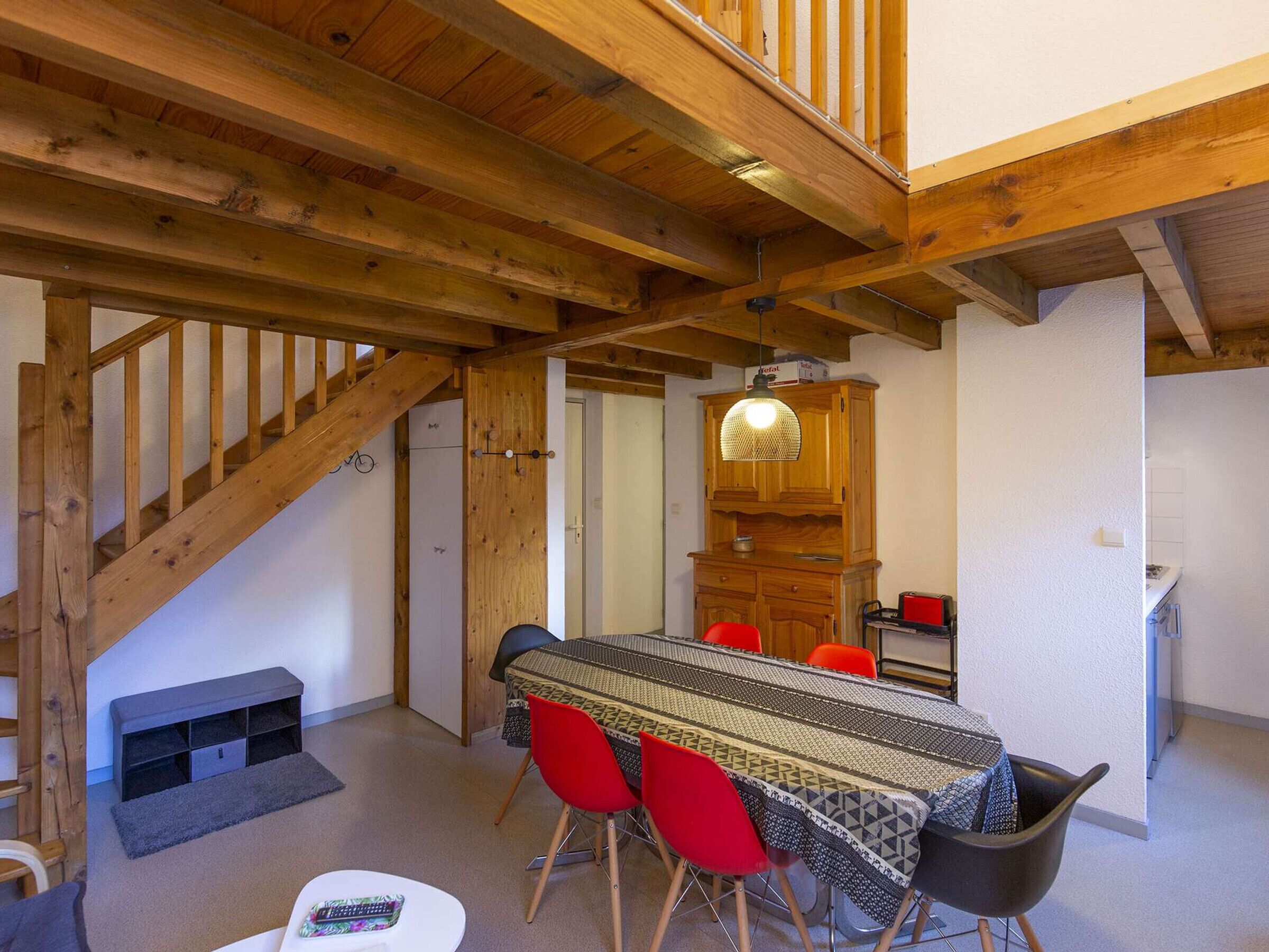 A dining area with a wooden ceiling, a staircase, and a kitchen area with a wooden cabinet and a hanging light fixture.