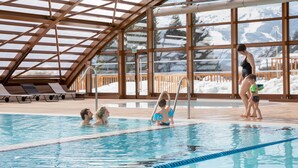 An indoor swimming pool with clear views of snow-covered mountains through large windows.