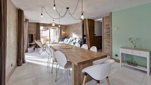 A modern kitchen with a wooden island, white chairs, and a hanging light fixture.