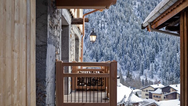 A wooden balcony with a metal railing overlooking a snow-covered mountain.