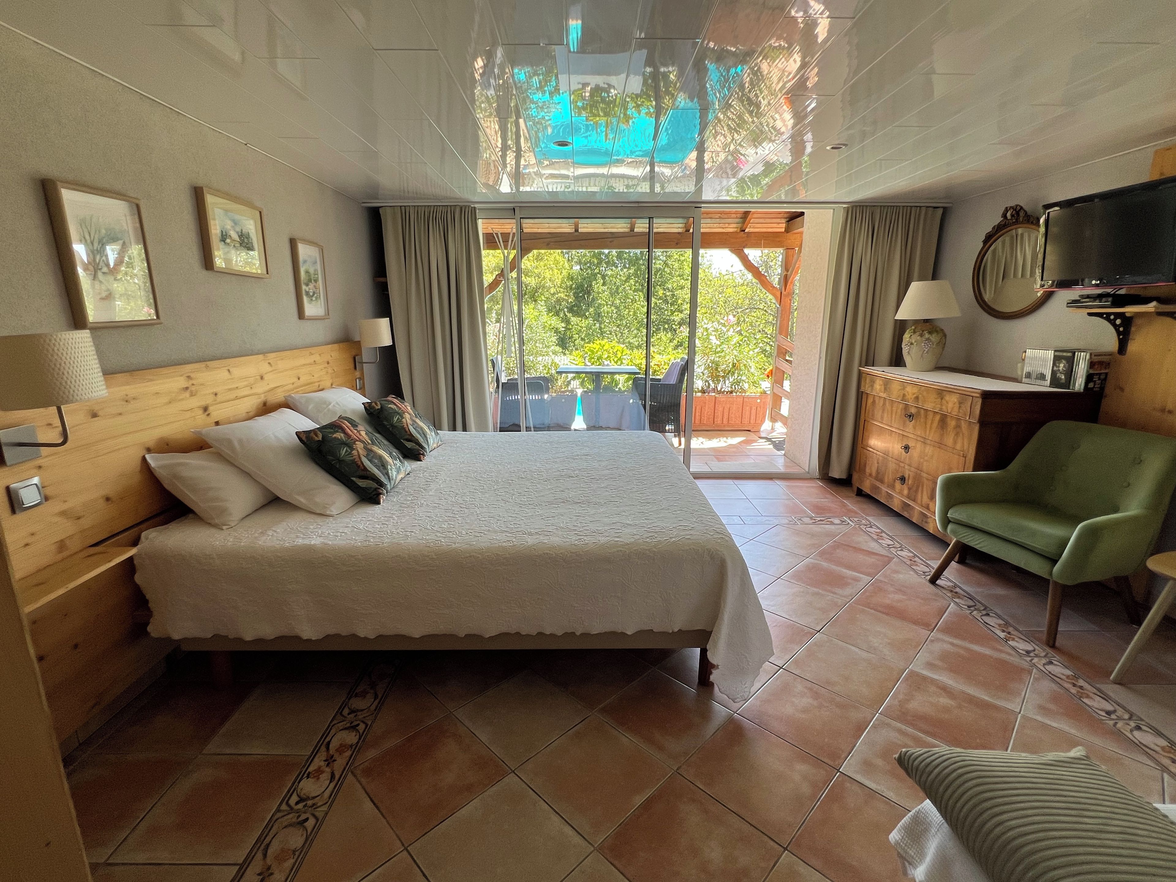Een hotelkamer met een bed, een groene fauteuil, een houten dressoir, een televisie en uitzicht op de omgeving.