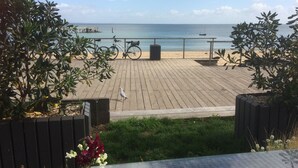 A wooden deck with a view of the beach and ocean, bicycles parked, and a seagull on the deck.