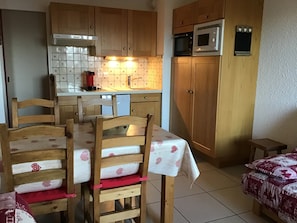 Une cuisine compacte avec des meubles en bois, un four à micro-ondes et une machine à café. On y trouve une table à manger avec des chaises et un petit tabouret.