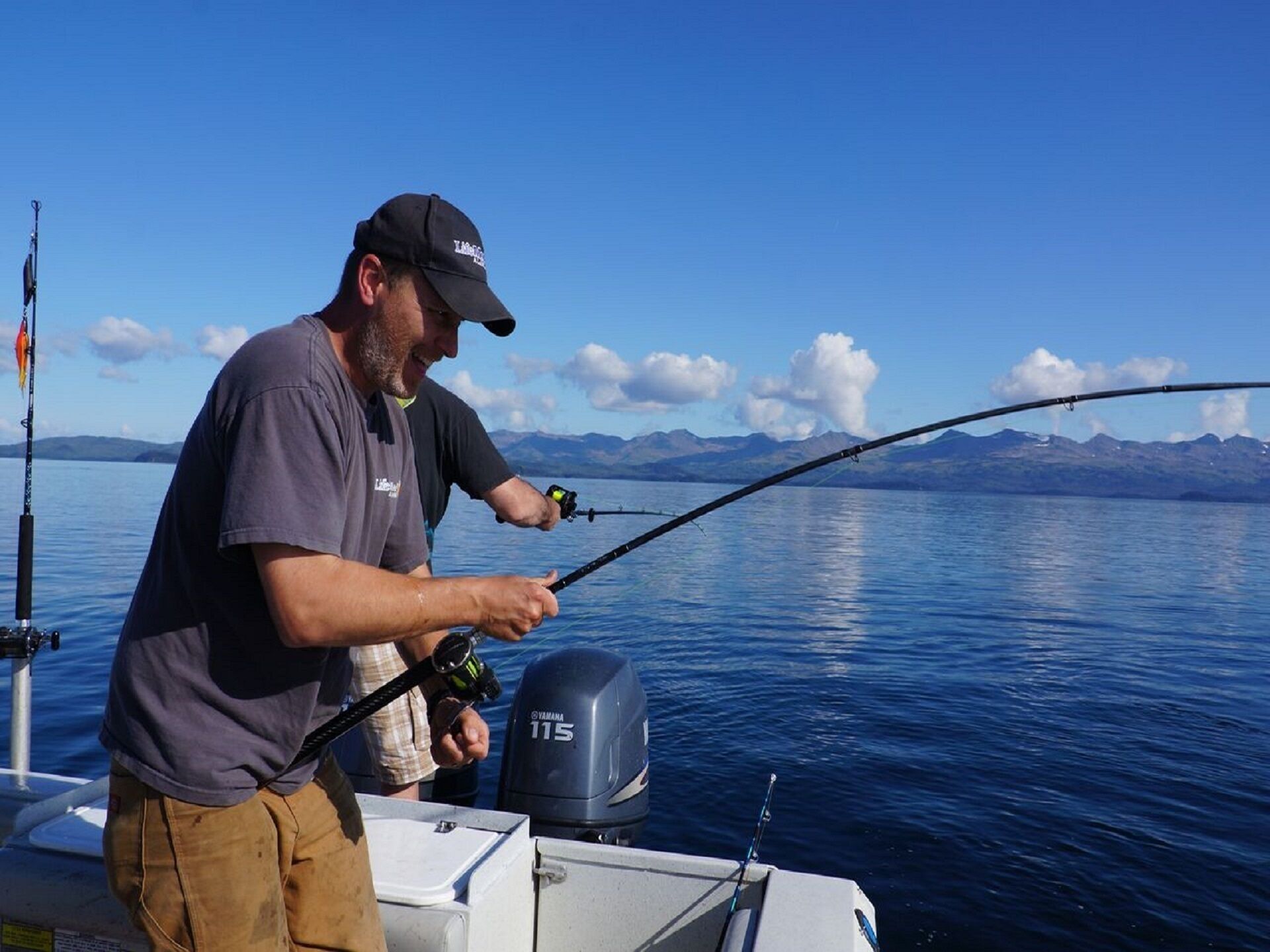 A person fishing on a boat with a clear view of mountains in the background.