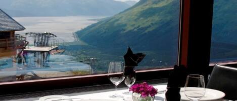 A table set for dining with a view of a mountainous landscape and a body of water.