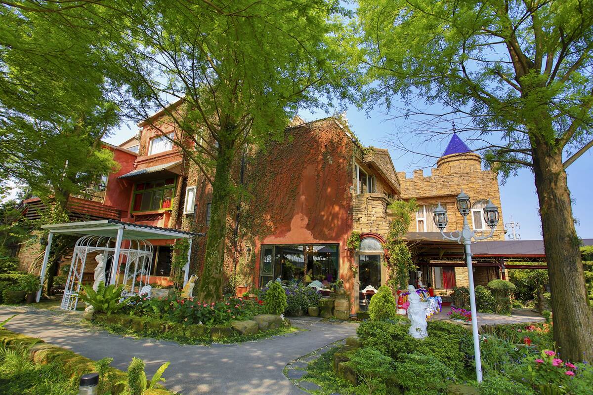A historic building with a turret and ivy-covered walls, surrounded by lush greenery and a pathway leading to the entrance.