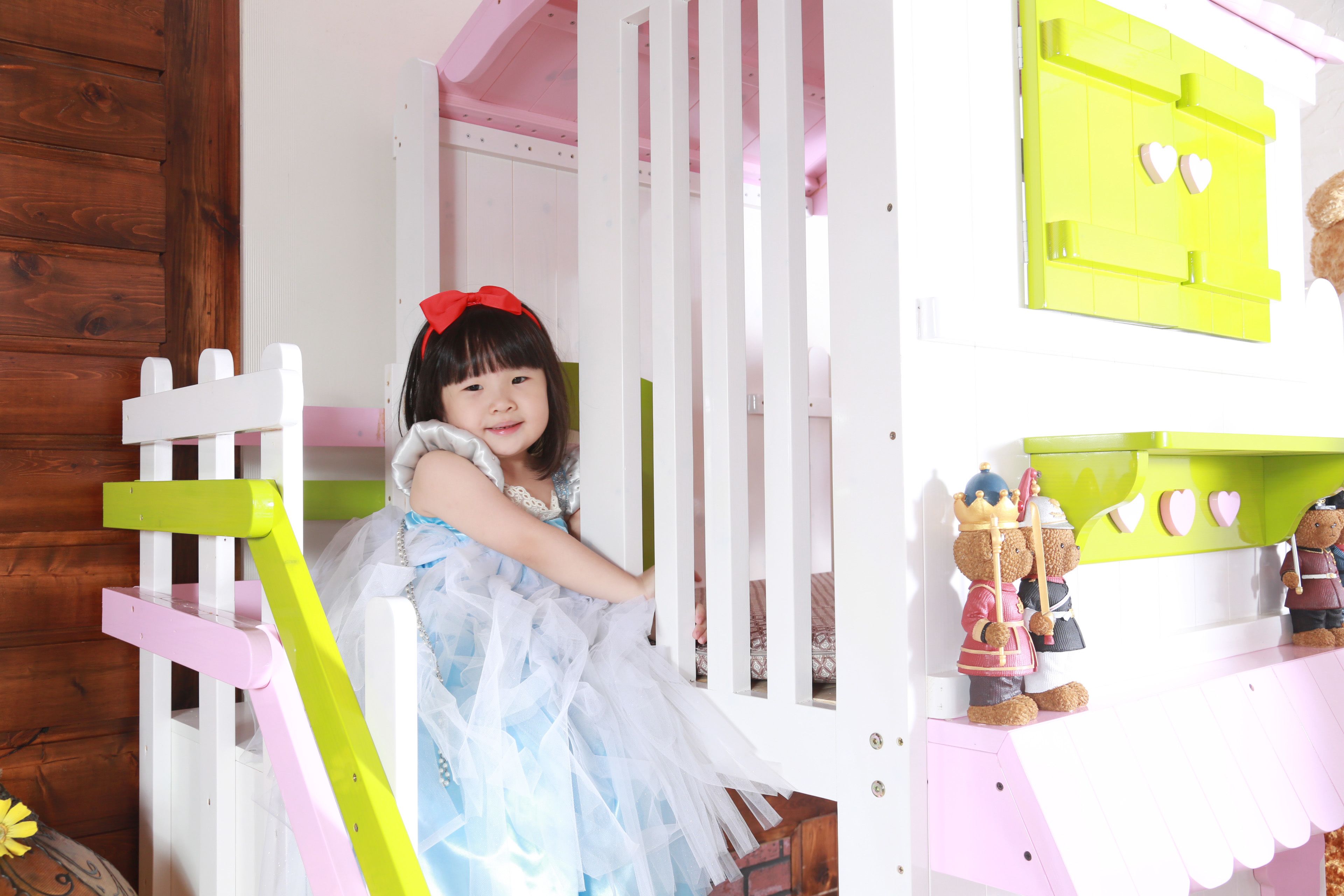 A child in a white dress with a red bow standing in a playhouse doorway.