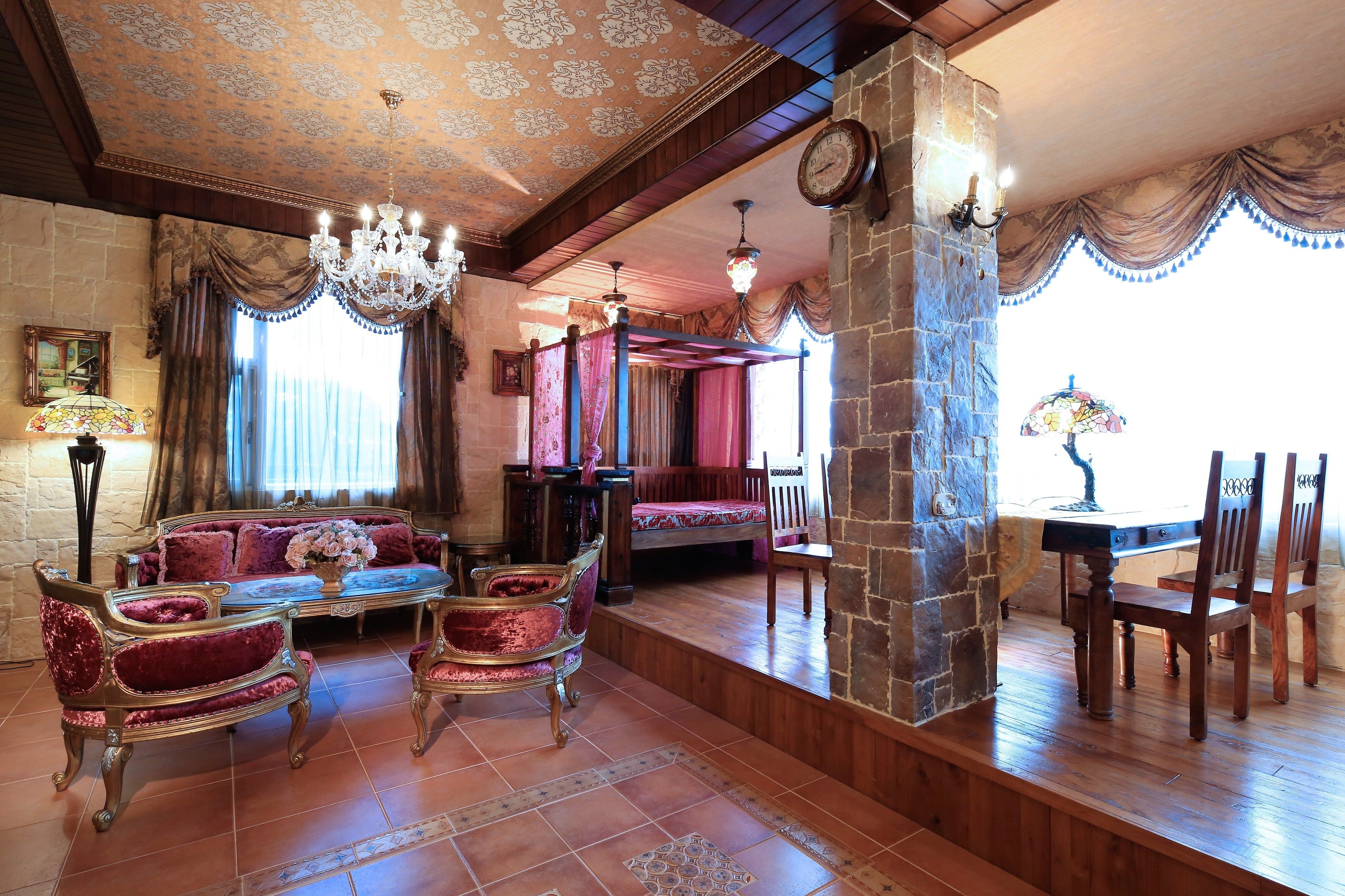 A room with a chandelier, a sofa, a dining table with chairs, and a stone pillar.
