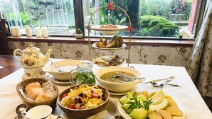 Mesa servida con diferentes platos, como sopa, ensalada y fruta, con vistas al verdor exterior.