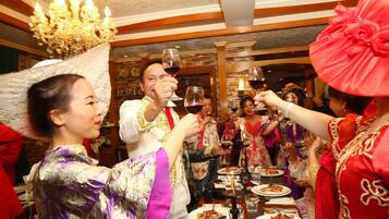 A group of people toasting with wine glasses at a dinner table in a room with wooden beams and a chandelier.